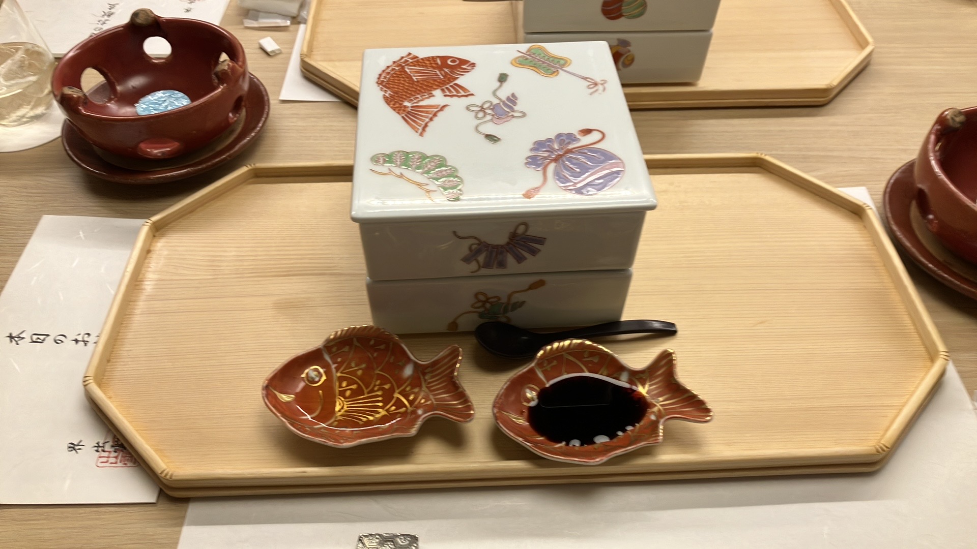 宝楽盛りの重箱。打ち出の小槌と同じように白っぽいベージュの下地に鯛や松、軍配、巾着、貝などが描かれている。手前には鯛の醤油皿